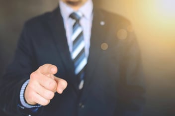 Close-up of a business professional in a suit pointing directly at the camera, symbolizing a call to action for anesthesiologists to take the lead in addressing the growing demand for spinal leak care. The gesture emphasizes the opportunity for anesthesiologists to enter a trillion-dollar market by offering long-term, patient-centered care for underdiagnosed conditions like post-dural puncture headaches and chronic spinal leaks.