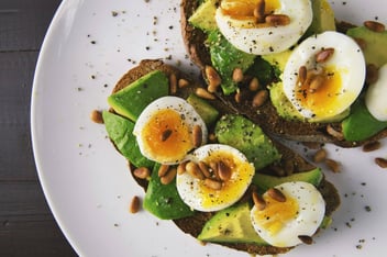 Hardboiled eggs cut in half sit on a bed of salad on a white plate, demonstrating a focus on nutrition.